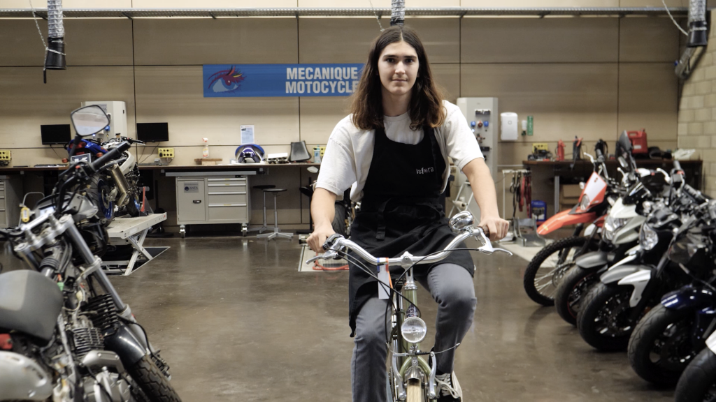 Apprenti dans un garage de motocycles sur un vélo entouré de motos apprenant le métier de mécanicien en motocycles.