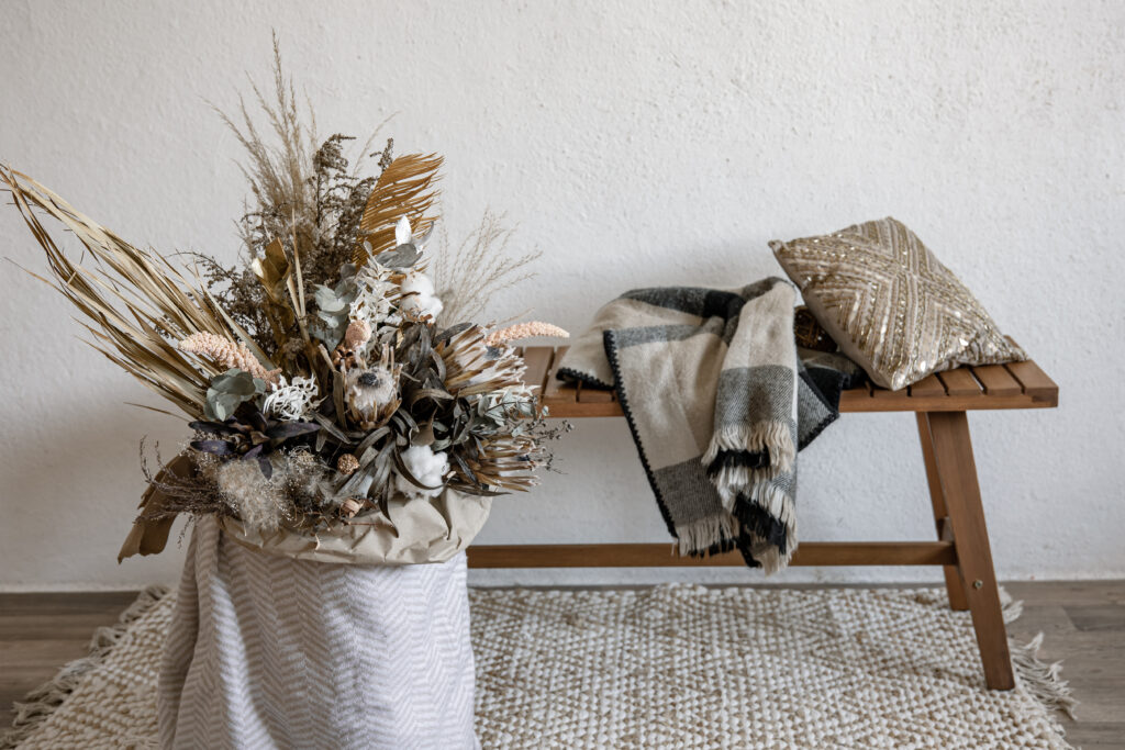 Décoration de Noël scandinaves avec une composition florale en matériaux naturels, banc en bois, plaid et coussin pour une ambiance chaleureuse.