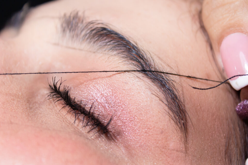 Gros plan sur une épilation des sourcils au fil sur une paupière fermée.
