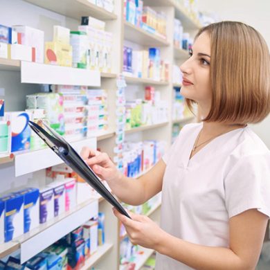 Femme devant un rayon de pharmacie, tenant un document permettant de préparer des commandes.