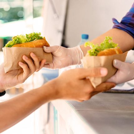 Zoom sur des mains distribuant un tacos provenant d'un foodtruck dans le cadre d'une restauration rapide.