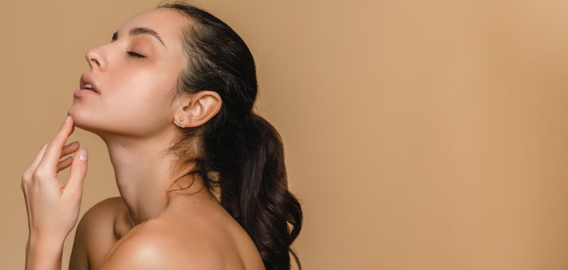 Photo of gorgeous beautiful young hispanic latin woman with clean fresh skin touching her face chin closed eyes over beige background side view close up. Cosmetology , beauty and spa concept.