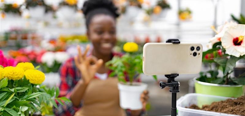 Fleuriste : développer sa visibilité grâce aux réseaux sociaux Fleuriste créant du contenu pour les réseaux sociaux en filmant ses compositions florales dans sa boutique.