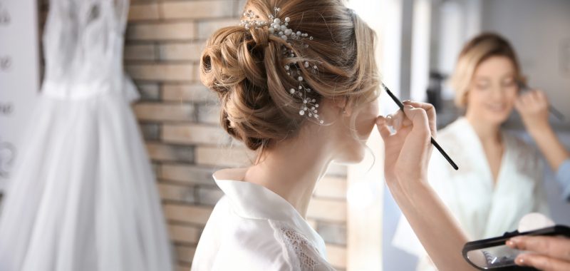 Makeup artist preparing bride before her wedding in room