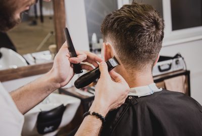 Young man with trendy haircut at barber shop. Barber does the hairstyle and beard trim. Concept barbershop.