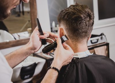 Young man with trendy haircut at barber shop. Barber does the hairstyle and beard trim. Concept barbershop.