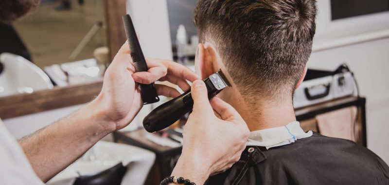 Young man with trendy haircut at barber shop. Barber does the hairstyle and beard trim. Young man with trendy haircut at barber shop. Barber does the hairstyle and beard trim. Concept barbershop.