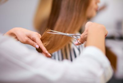 rear view on cropped careful hairdresser cutting off long hair of client with scissors, in beauty salon
