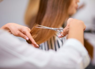 rear view on cropped careful hairdresser cutting off long hair of client with scissors, in beauty salon