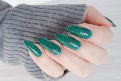 Female hand with long nails and green manicure with bottles of nail polish