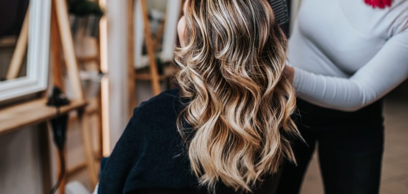 Beautiful hairstyle of young woman after dyeing hair and making highlights in hair salon.