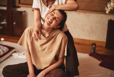 Attractive woman sitting in excitement from Thai massage of her shoulder that she getting from specialist behind her