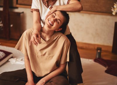 Attractive woman sitting in excitement from Thai massage of her shoulder that she getting from specialist behind her