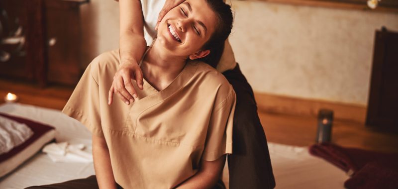 Attractive woman sitting in excitement from Thai massage of her shoulder that she getting from specialist behind her