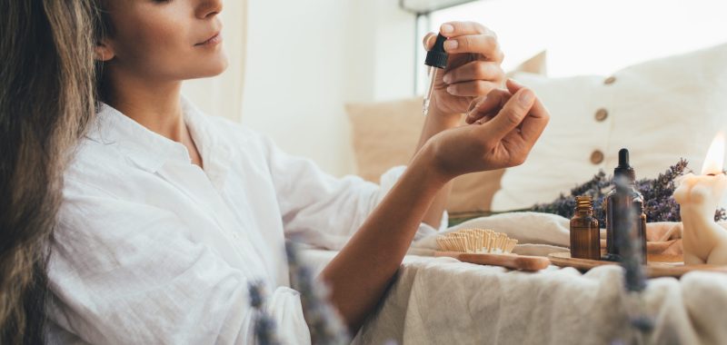 Young woman applying natural organic essential oil on hair and skin. Home spa and beauty rituals. Skin care.