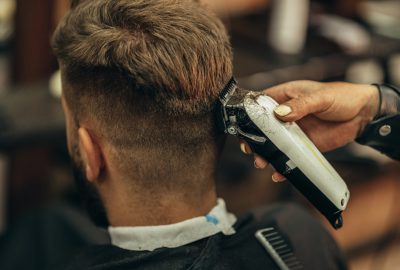 Young bearded man getting haircut by hairdresser while sitting in chair at barbershop
