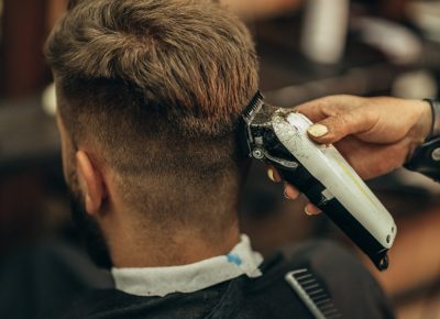 Young bearded man getting haircut by hairdresser while sitting in chair at barbershop