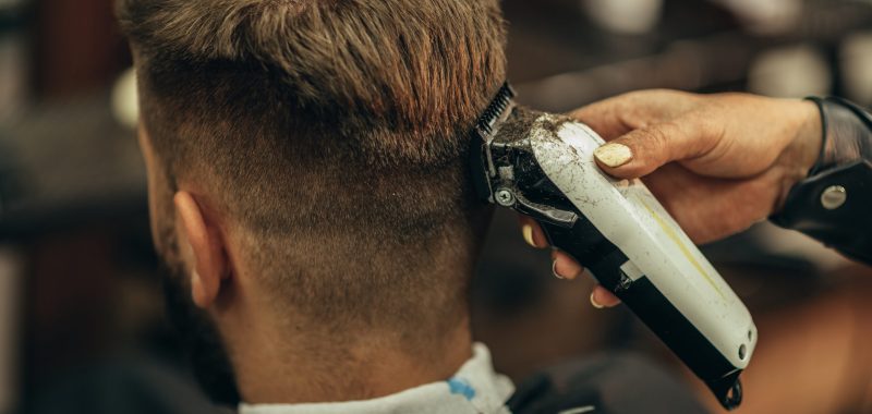 Young bearded man getting haircut by hairdresser while sitting in chair at barbershop