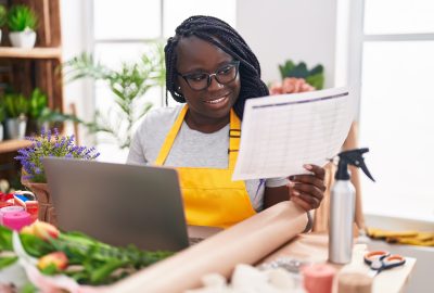 African american woman florist using laptop reading document at florist