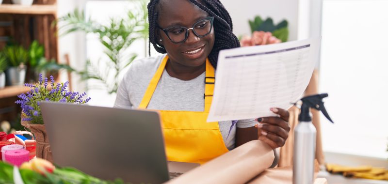 African american woman florist using laptop reading document at florist