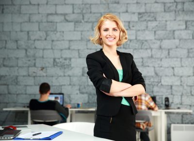 Young happy businesswoman with arms folded standing in office