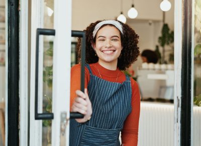 Portrait, welcome and woman at coffee shop door for opening with friendly smile of hospitality. Cafe, entrance and retail with happy restaurant owner or waitress at store for greeting or service.