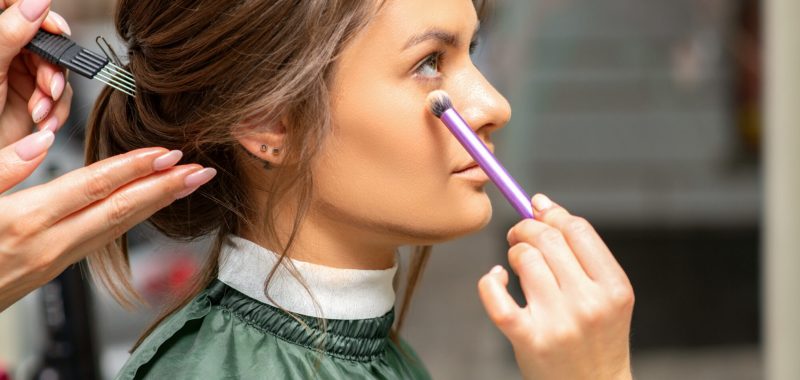Makeup and hairstyle process. Makeup artist and hairdresser preparing young caucasian woman, working in tandem
