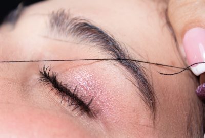 Gros plan sur une épilation des sourcils au fil sur une paupière fermée.