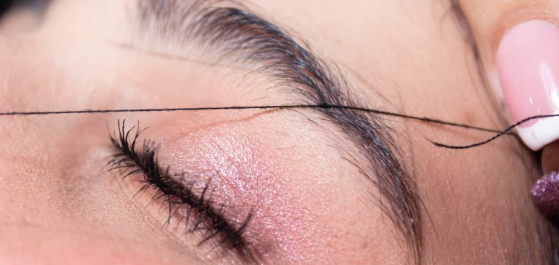 Gros plan sur une épilation des sourcils au fil sur une paupière fermée.