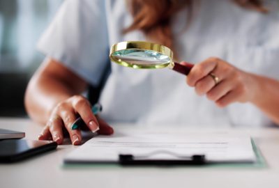 Femme analysant un document sur les prix en coiffure et esthétique avec une loupe