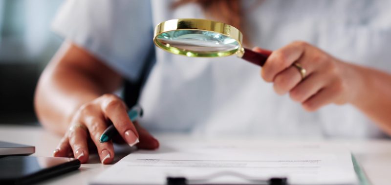 Analyse du prix en coiffure et esthétique pour une meilleure rentabilité Femme analysant un document sur les prix en coiffure et esthétique avec une loupe